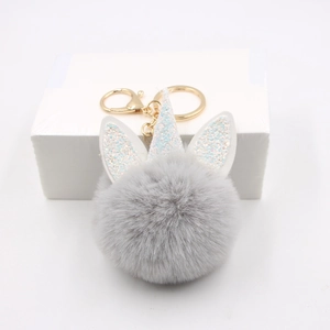 Unicorn plush pom pom keychain with grey faux fur and golden glitter horn on white box