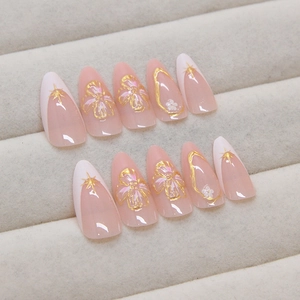 French tip press-on nails with golden floral patterns and stars on a nude pink base