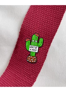 Detail of cactus enamel pin with 'DON'T BE A PRICK' text on woven fabric background