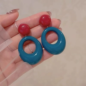 Detail of red resin studs and blue oval hoop earrings held for close-up view