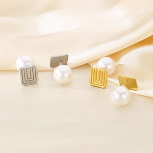 Detail view of square gold and silver pearl earrings on soft beige silk background