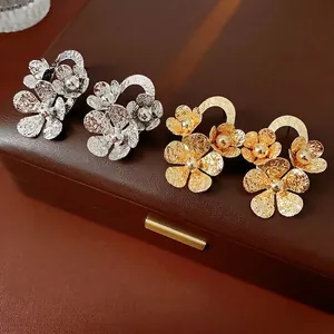 Textured gold and silver layered flower stud earrings on leather jewelry case