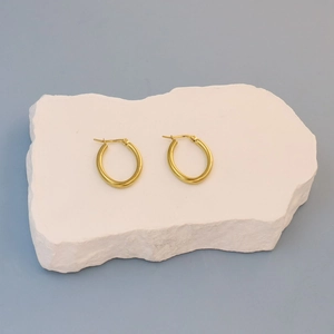 Detail of gold flat hoop earrings on a textured stone surface with a matte finish