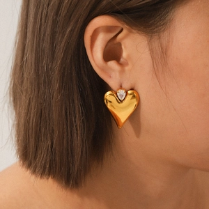 Macro shot of gold heart stud earring with teardrop zircon on woman's ear