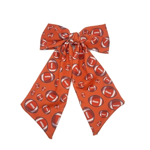 Detail of an orange hair bow clip featuring American football prints and long ribbons