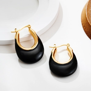 Detail of U-shaped gold earrings with black enamel finish on a minimalist display
