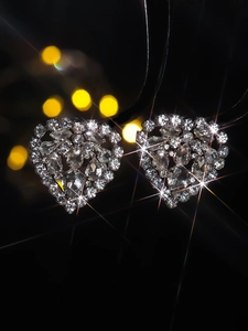 Macro shot of silver heart earrings with sparkling glass crystals on black background