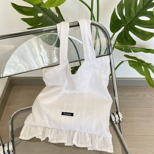 Close-up of a white canvas tote bag featuring vertical stripes and ruffled hem details