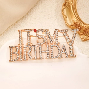 Detailed view of 'IT'S MY BIRTHDAY' gold brooch with clear and red sparkling rhinestones