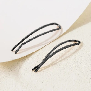 Close-up of minimalist black metal hair clips with smooth finish and textured pattern detail
