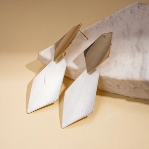 Detailed macro view of geometric diamond earrings with brushed gold and silver metal textures