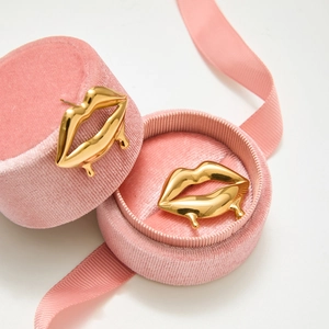 Détail de boucles d'oreilles lèvres dorées sur boîte en velours rose avec ruban