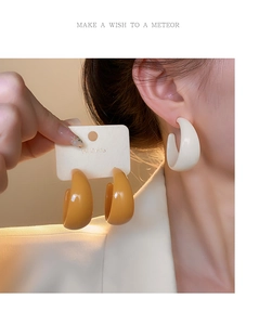 Detail view of large C-shaped acrylic earrings in cream white and mustard yellow