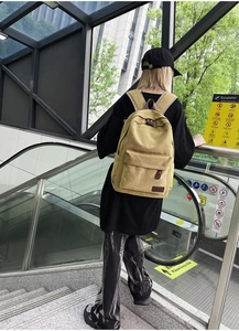 Detailed view of yellow canvas backpack with leather buckle on male model's back