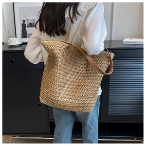Detailed texture of large straw tote bag featuring brown leather handles and handwoven fibers
