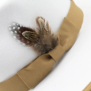 Detail of white wool felt fedora featuring grosgrain ribbon and natural feather accents