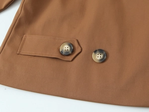 Detail of brown trench coat featuring tortoiseshell buttons and rectangular patch fabric