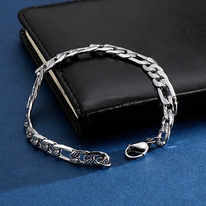 Close-up of a silver Figaro chain bracelet with lobster clasp on a black leather notebook