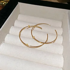 Minimalist gold-tone irregular hoop earrings with pyramid stud details on a velvet tray