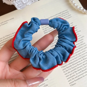 Detailed macro of blue denim scrunchie with red pleated edges and purple ornament