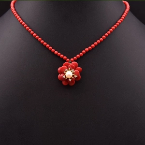 Detailansicht einer roten Perlenkette mit Blumenanhänger und Perle auf einer schwarzen Büste