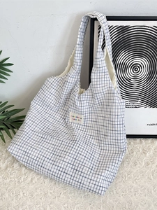Minimalist blue checkered canvas tote bag with wide shoulder strap on a white plush rug