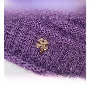 Dettaglio del cappello in maglia viola con una spilla a quadrifoglio di strass
