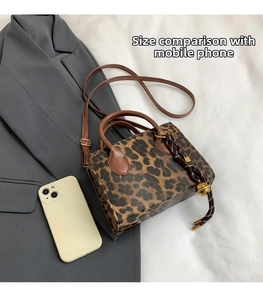 Detail of leopard print crossbody bag featuring gold bell charm on a grey blazer