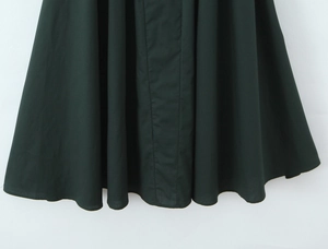 Detailed view of the dark green dress hem showing elegant fabric drape and pleats