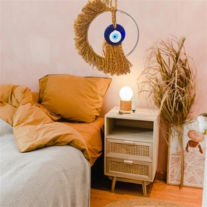 Detail of macrame woven wall hanging with blue evil eye bead in a cozy bedroom setting