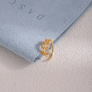 Detailed view of a gold leaf nose stud with white cubic zirconia on blue velvet