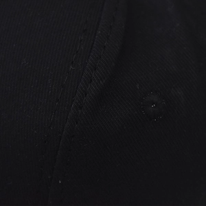 Gros plan du tissu sergé de coton noir avec coutures renforcées et œillet de la casquette