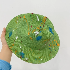 Green straw sun hat with unique colorful paint splatter design for a stylish summer look