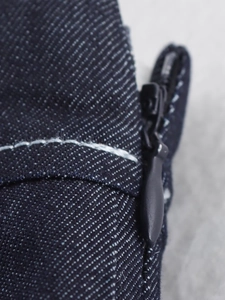 Dettaglio ravvicinato di denim blu scuro con cuciture bianche e zip nera a scomparsa