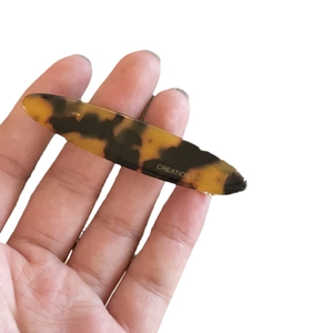 Amber tortoiseshell acetate hair clip with gold lettering held in hand on white background