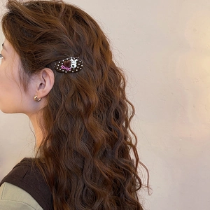 Detail of brown polka dot hair clip with Zsiga cartoon design on wavy hair