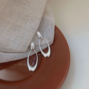 Minimalist silver geometric oval earrings displayed on a rustic ceramic plate
