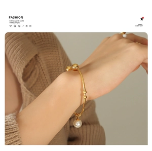 Detailed view of an 18K gold-plated minimalist bracelet with white pearl charm on wrist