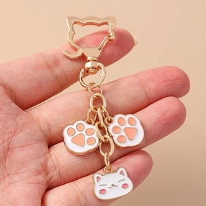 Cute cartoon golden cat and paw enamel pendants keychain held against a beige background