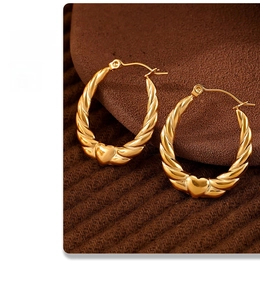 Macro view of gold-plated twisted C-shaped earrings with delicate heart charm detail