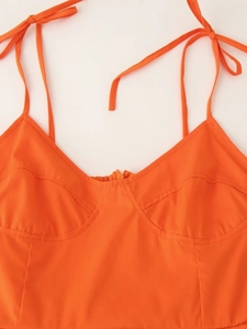 Detail van een oranje jurk met geknoopte schouderbandjes en gestructureerd lijfje