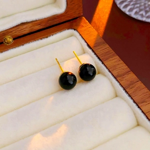 Vue macro de boucles d'oreilles perles grises avec tiges dorées sur coussin blanc