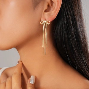 Close-up of 18K gold plated bow earrings with zircon and triple chain tassels on model