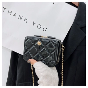Detail of a black quilted PVC jelly bag featuring a golden camellia logo and chain
