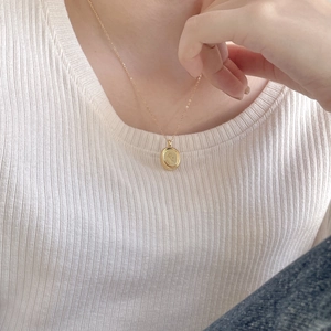 Close-up of golden oval pendant necklace with floral rose engraving worn on neck