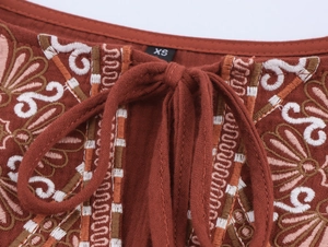 Detailed close-up of ethnic embroidery and lace-up neck on rust red cotton linen dress