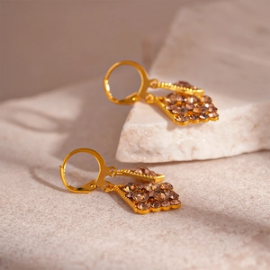 Close-up of gold geometric drop earrings with amber crystals on a natural stone base