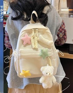 Detail of cream canvas backpack featuring plush star ornaments and a cute bear keychain