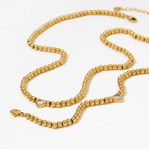Collier à billes dorées avec pendentif en cristal en forme de cœur sur fond blanc