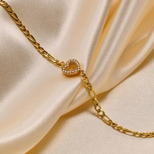 Detail of 18K gold Figaro chain bracelet with heart pendant and white zircon inlay